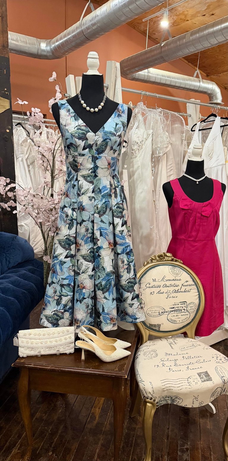 Boutique display with mannequins wearing dresses, vintage furniture, and accessories under industrial ceiling