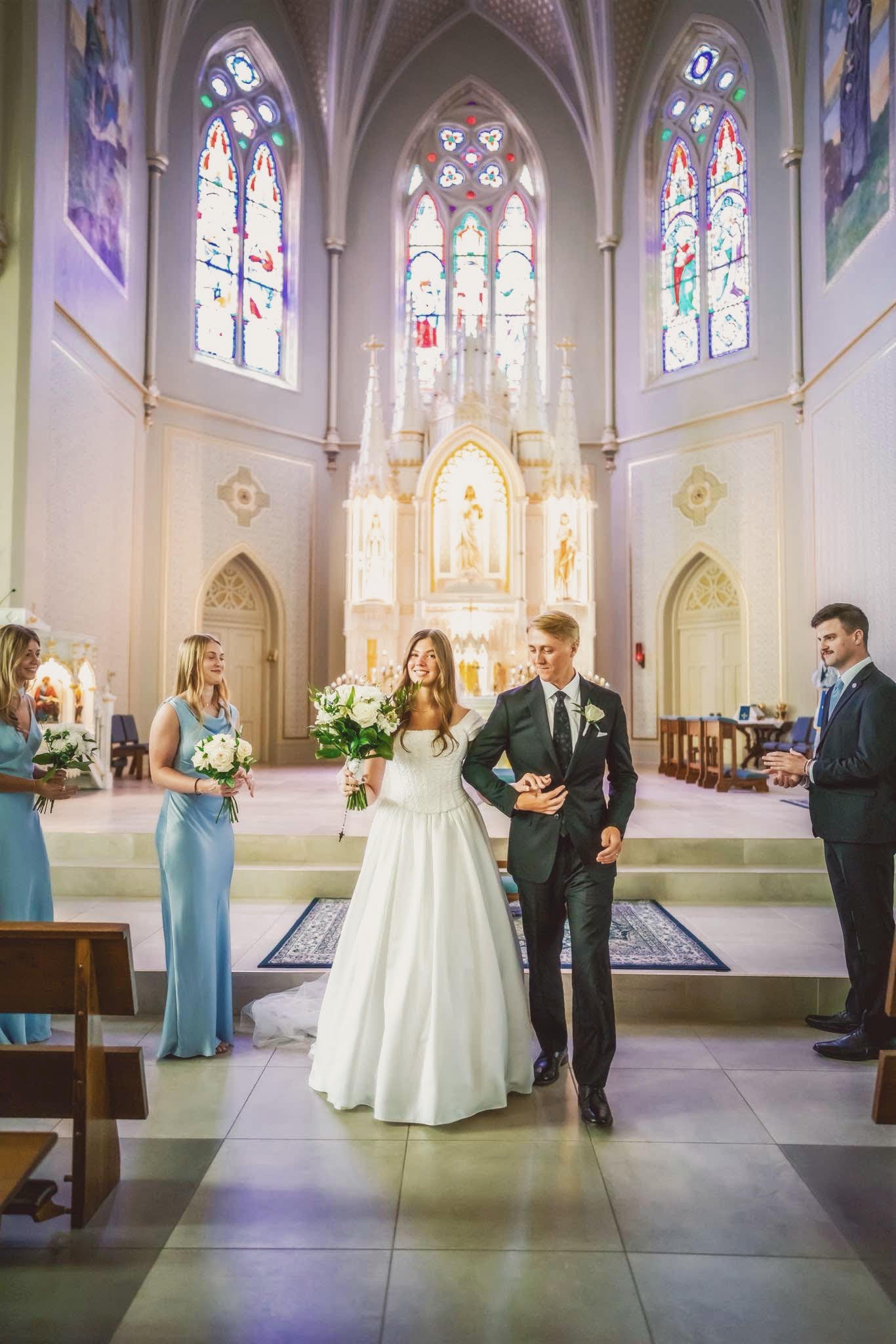 Bride and groom walking down the aisle in a Gothic cathedral with stained glass windows during wedding ceremony